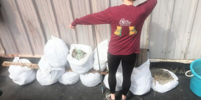 Woman standing with her back to the camera pointing at a pile of filled white trash bags.