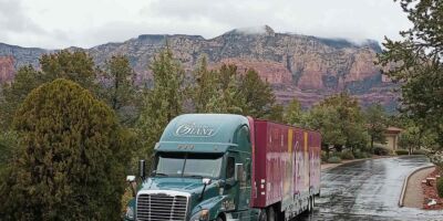 An interstate Gentle Giant moving truck is parked on a tree lined road. Behind it is a view of the red rock landscape of Sedona.