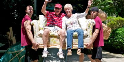 Seniors sitting on a couch being carried by professional movers during a home relocation.